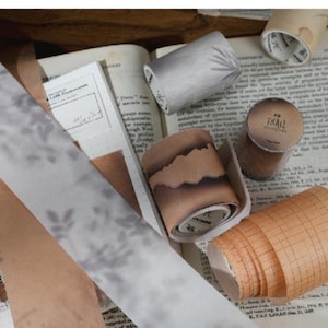 May include: A collection of washi tapes in different designs, including floral, grid, and solid patterns. The tapes are shown with vintage paper ephemera, pencils, and scissors, creating a scrapbook or journaling theme.