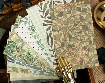 May include: A set of eight decorative paper sheets featuring a variety of floral and leaf patterns in shades of green, white, and brown. The papers are arranged in a fan shape and have a vintage aesthetic.