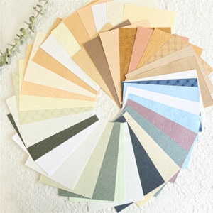 May include: A fan-shaped arrangement of different textured paper samples in various shades of beige, brown, blue, and grey.