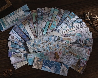 Puede incluir: Un conjunto de pegatinas decorativas de estilo vintage en tonos azules y blancos. Las pegatinas tienen una variedad de diseños, incluyendo conchas marinas, sirenas y temas náuticos. Las pegatinas están empaquetadas en una caja azul con el texto "Retro Material Sticker" en la parte delantera.