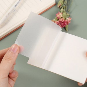 May include: A white notepad with a clear plastic cover. The cover is partially peeled back to reveal the blank pages inside.