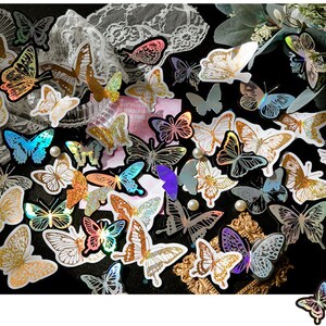 May include: Assortment of iridescent butterfly stickers with holographic glitter accents. The stickers are arranged in a random pattern on a black background.