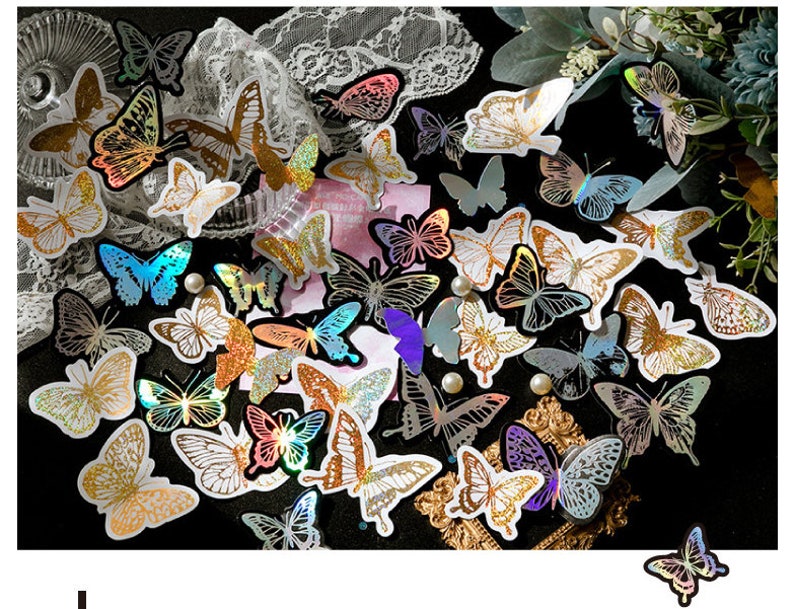 May include: Assortment of iridescent butterfly stickers with holographic glitter accents. The stickers are arranged in a random pattern on a black background.