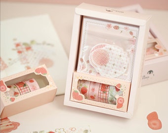 May include: A set of four pink and white washi tapes with strawberry designs, packaged in a pink box with a clear window. The box also includes a pink and white patterned sticker sheet.