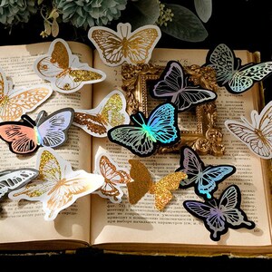 May include: Assortment of iridescent butterfly stickers in various colours, including gold, silver, blue, pink, and green. The stickers are arranged on a book with text in Russian.