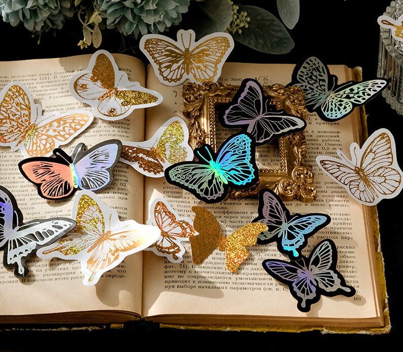 May include: Assortment of iridescent butterfly stickers in various colours, including gold, silver, blue, pink, and green. The stickers are arranged on a book with text in Russian.