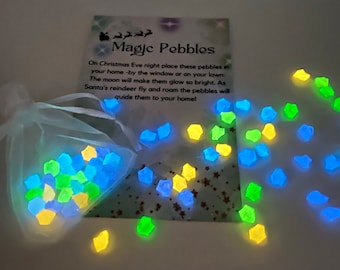 May include: A small white organza bag filled with glowing green, blue, and yellow pebbles. The bag is next to a card that reads "Magic Pebbles" and explains that the pebbles will glow when placed outside on Christmas Eve to guide Santa's reindeer.