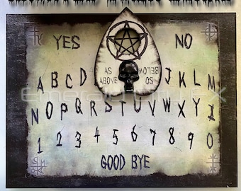May include: A wooden Ouija board with a black skull planchette. The board has a white background with black lettering and numbers. The board says "HAUNTED OUIJA BOARD" at the top and "WITH SKULL PLANCHETTE" at the bottom. The board has the letters A-Z, numbers 1-0, and the words "YES", "NO", "GOOD BYE", and "AS ABOVE, SO BELOW".