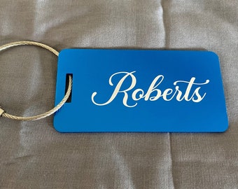 May include: Blue luggage tag with a silver metal loop and the name "Roberts" engraved in white.