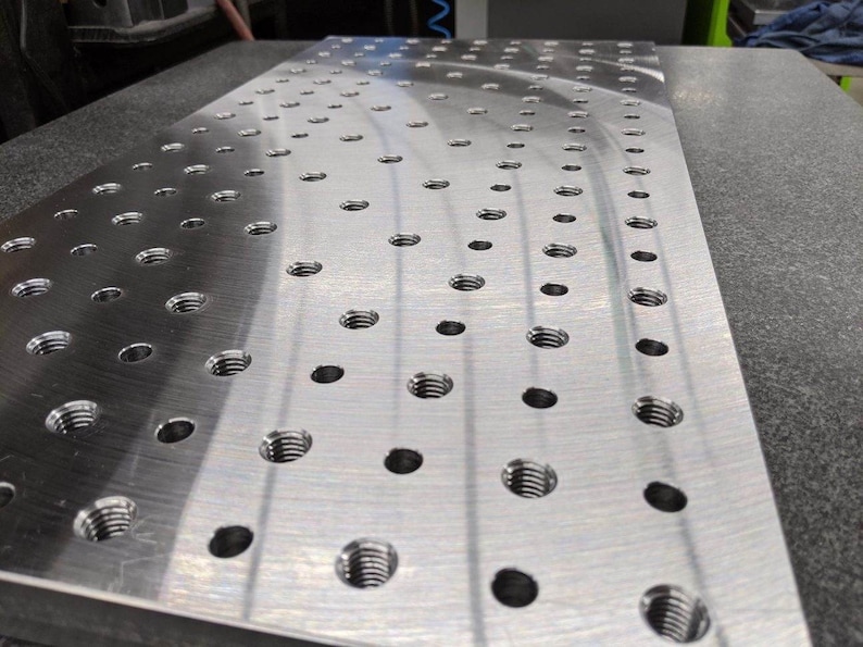 May include: A silver metal plate with a grid of evenly spaced holes. The plate is smooth and reflective, and the holes are arranged in a pattern that creates a visual texture.