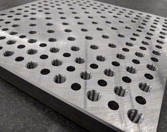 May include: A silver metal plate with a grid of evenly spaced circular holes. The holes are threaded and appear to be used for fastening.