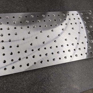May include: A silver metal plate with a grid of evenly spaced circular holes. The plate is smooth and reflective.