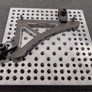 May include: A metal plate with a grid of holes, a metal bracket, and two clamps. The bracket is secured to the plate with the clamps.