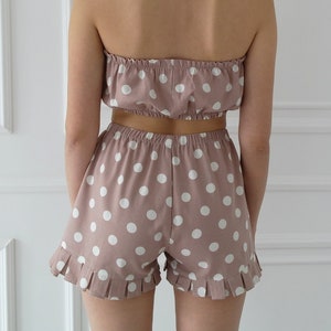 May include: A pink and white polka dot crop top and matching shorts. The top is strapless and the shorts have a ruffled hem.