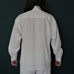 May include: A white long-sleeved button-up shirt with a collar and a single button at the top.