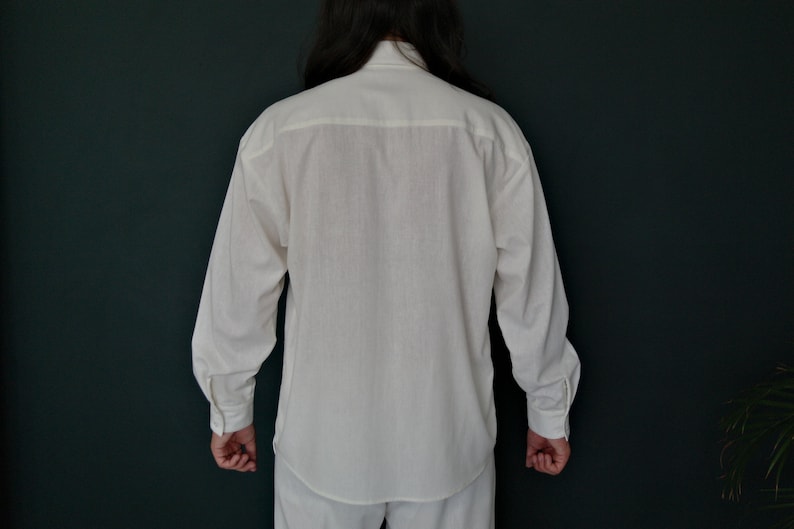 May include: A white long-sleeved button-up shirt with a collar and a single button at the top.