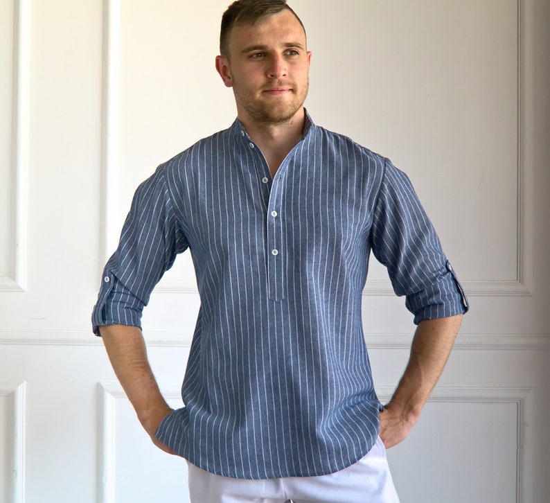 May include: Blue and white striped Henley shirt with a mandarin collar and three-quarter sleeves. The shirt has a button-down placket and rolled-up sleeves. The shirt is made of a lightweight fabric.