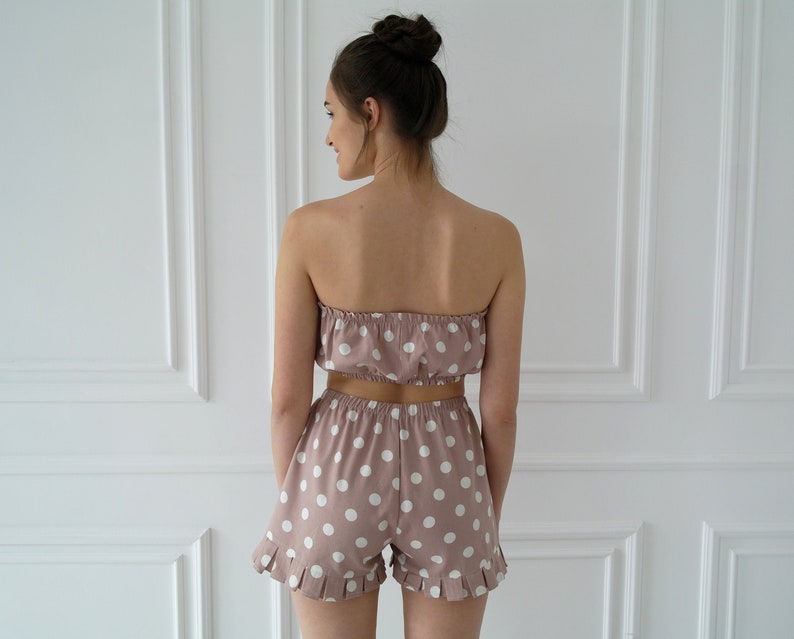 May include: A pink and white polka dot crop top and matching shorts. The top is strapless and the shorts have a ruffled hem.
