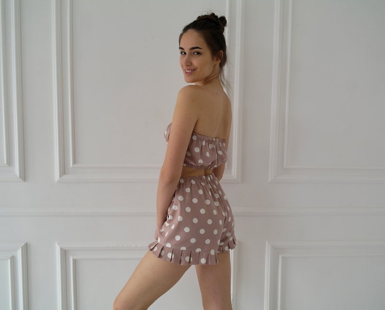 May include: A pink and white polka dot pajama set with a strapless top and shorts. The shorts have a ruffled hem.