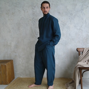 Pode incluir: Um conjunto de camisa e cal&ccedil;as de linho azul-petr&oacute;leo. A camisa tem gola alta e mangas compridas. As cal&ccedil;as s&atilde;o largas e de perna reta.