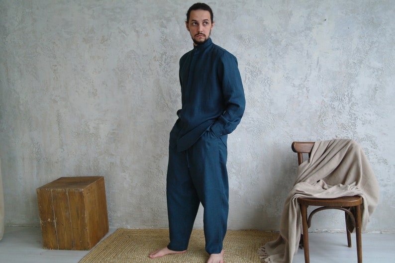 Pode incluir: Um conjunto de camisa e cal&ccedil;as de linho azul-petr&oacute;leo. A camisa tem gola alta e mangas compridas. As cal&ccedil;as s&atilde;o largas e de perna reta.