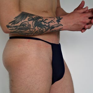 May include: A person wearing a dark blue thong style underwear. The underwear has a thin strap that goes around the waist and ties at the front.