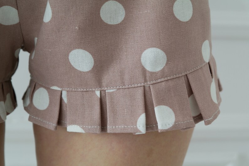 May include: Close-up of the hem of a pair of brown shorts with white polka dots. The hem has a ruffled edge.