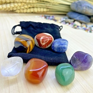 Peut inclure: Un assortiment de pierres précieuses polies de différentes couleurs, dont l'œil de tigre, le jaspe rouge, la sodalite bleue, l'améthyste, la cornaline, le quartz clair et l'aventurine verte. Les pierres sont présentées avec un sac noir à cordon.