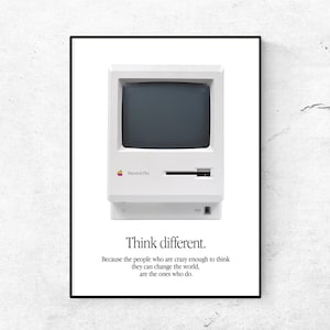Puede incluir: Un póster enmarcado con un ordenador Macintosh Plus vintage. El ordenador blanco tiene una pantalla oscura y una unidad de disquete. Debajo, el texto dice "Think different." y una cita sobre cambiar el mundo.