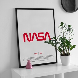 May include: A black framed poster with the NASA logo in red. The poster has the text "NASA | 1975" and a description of the logo's history.