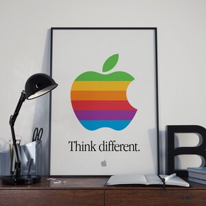 May include: A black framed poster with a rainbow colored Apple logo and the text "Think different." The logo is a stylized apple with a bite taken out of the right side.