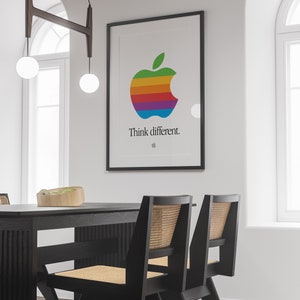 May include: A black framed poster with a rainbow colored Apple logo and the text "Think different." The poster is hanging on a white wall above a black dining table with two black chairs with woven cane seats.