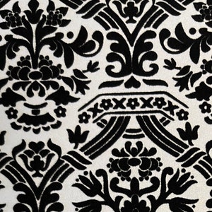 Puede incluir: Tela damasco en blanco y negro con un patrón repetitivo de flores y hojas estilizadas. La tela tiene una textura en relieve.