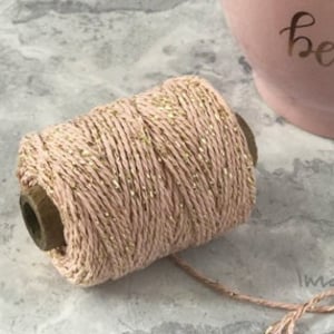 Peut inclure: Une bobine de ficelle rose avec des paillettes dorées. La ficelle est enroulée autour d'une bobine en bois.
