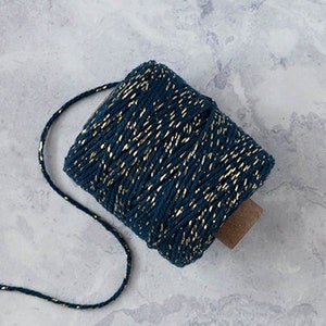 Peut inclure: Une bobine de ficelle bleu foncé avec du fil métallique doré qui la traverse. La ficelle est posée sur une surface en marbre blanc.