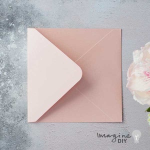 Puede incluir: Un sobre cuadrado de color rosa p&aacute;lido con una solapa rosa m&aacute;s clara. El sobre est&aacute; sobre una superficie gris, con una flor blanca en el fondo. El texto "Imagine DIY" es visible en la esquina inferior derecha.