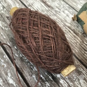 May include: A ball of brown twine with a wooden spool. The twine is tightly wound and has a rough texture.