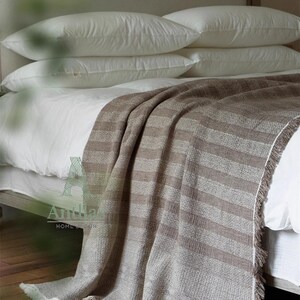 Pu&ograve; includere: Un letto con cuscini bianchi e una coperta a righe marrone e beige. La coperta ha un bordo con frange ed &egrave; drappeggiata sul letto. Il letto &egrave; fatto con lenzuola bianche.