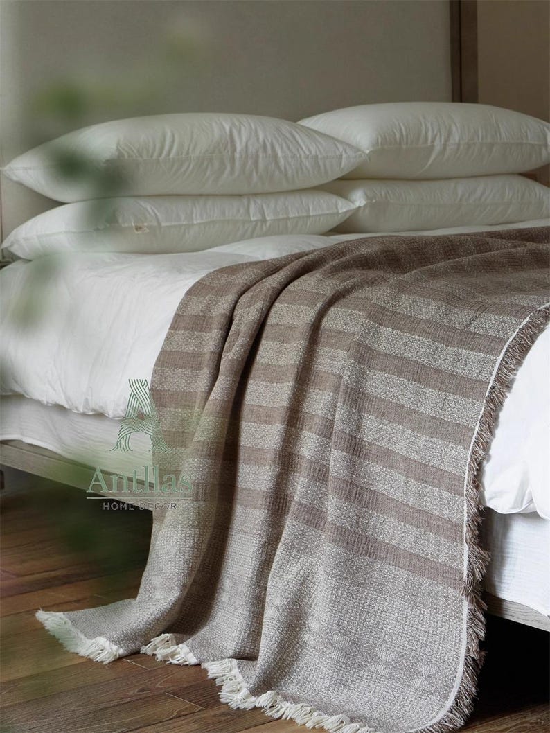 Pu&ograve; includere: Un letto con cuscini bianchi e una coperta a righe marrone e beige. La coperta ha un bordo con frange ed &egrave; drappeggiata sul letto. Il letto &egrave; fatto con lenzuola bianche.