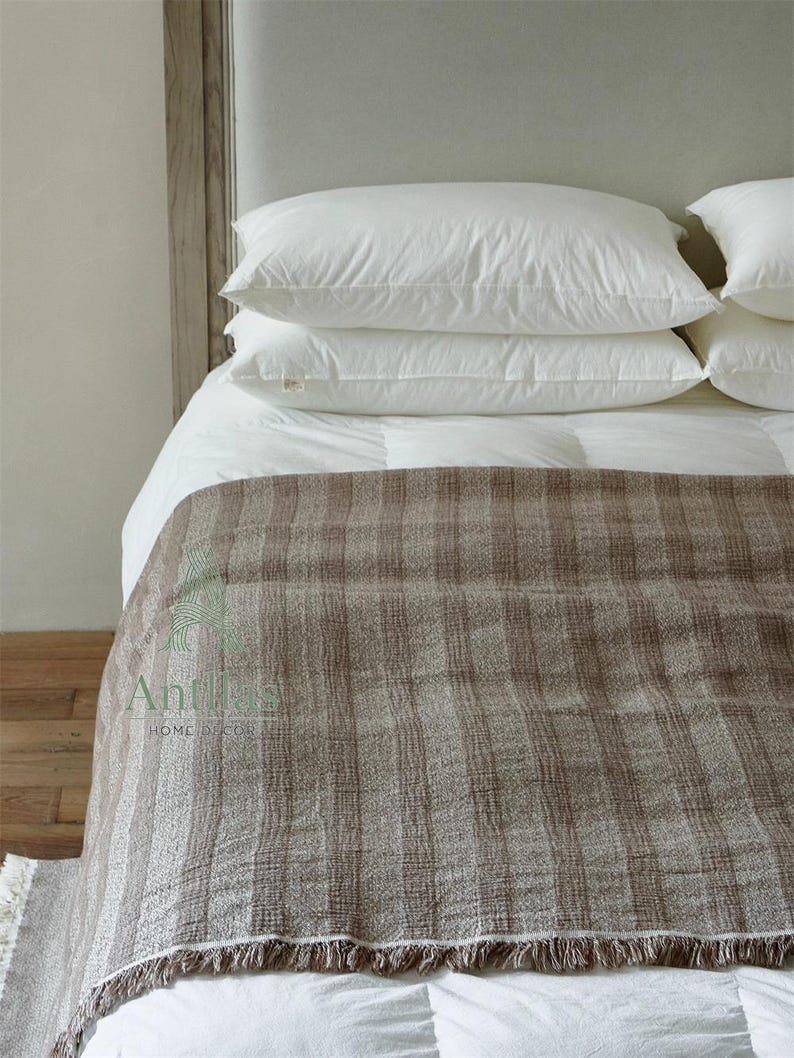 Pu&ograve; includere: Un letto con cuscini bianchi e una coperta a righe marrone e beige. La coperta ha un bordo sfrangiato ed &egrave; drappeggiata sul letto. Il letto &egrave; fatto con lenzuola bianche e un piumino bianco.