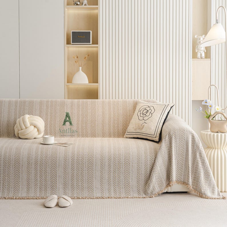 May include: Beige sofa with a patterned throw blanket and a decorative pillow featuring a rose design. A matching knot pillow, a cup, and slippers are on the sofa. The word "A" and the brand name "Antllas" are printed on the sofa.