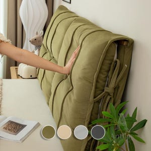 Può includere: Un cuscino per testata imbottito verde salvia è montato su un muro. Il cuscino ha cuciture a canale verticali e una chiusura annodata. L'immagine mostra anche un letto dai toni neutri, una lampada decorativa e un peluche.