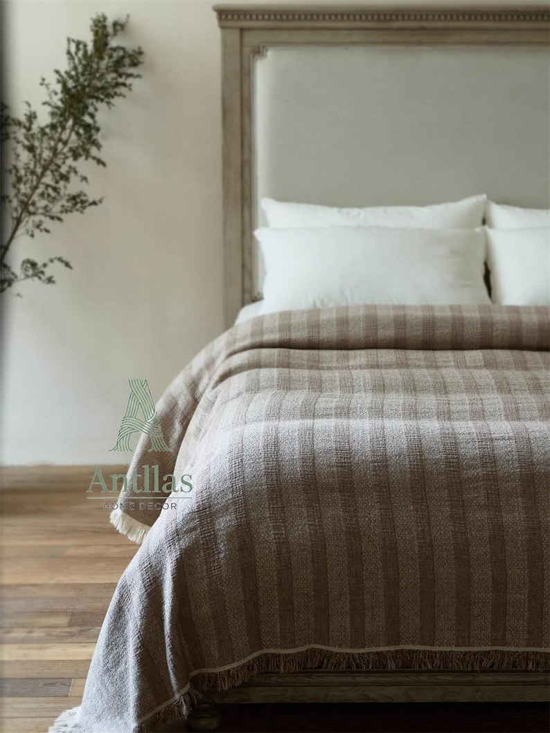 Pu&ograve; includere: Un letto &egrave; coperto da una coperta a righe marrone e beige. La coperta ha una frangia lungo il bordo inferiore. Cuscini bianchi poggiano sul letto e la testiera &egrave; di colore beige chiaro. L'immagine &egrave; di una camera da letto.