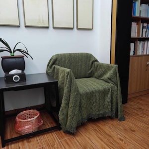 May include: A green patterned throw blanket draped over an armchair. The blanket has a chevron design and fringe along the bottom. The words "Real customer scene" are at the bottom of the image.