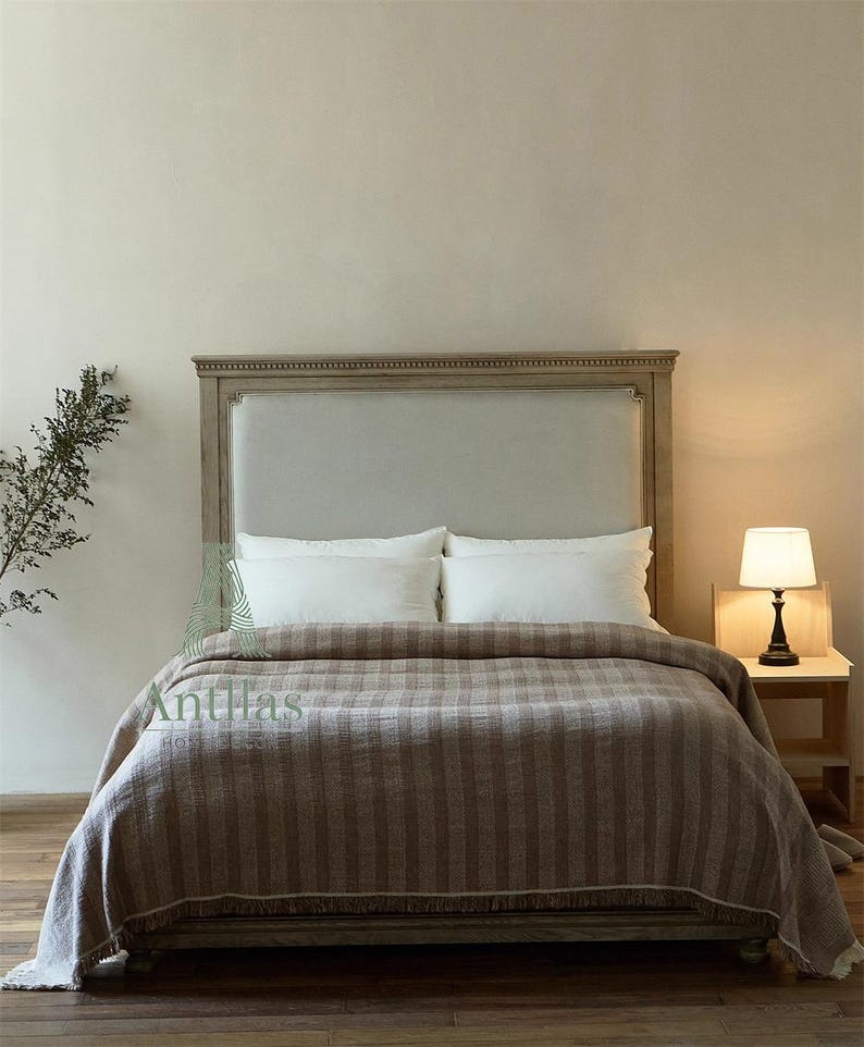 Pu&ograve; includere: Un letto con testiera in legno chiaro e una coperta a righe marroni. Il letto &egrave; fatto con cuscini bianchi e un copriletto abbinato. Una piccola lampada &egrave; su un comodino accanto al letto. La parola "Antillas" &egrave; visibile.