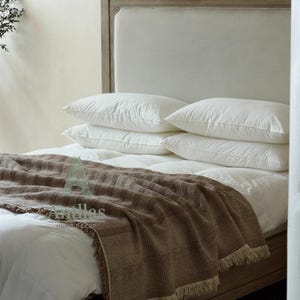 Pu&ograve; includere: Un letto con struttura e testiera in legno chiaro. Il letto &egrave; fatto con biancheria da letto bianca, compresi cuscini e un piumino. Una coperta marrone intrecciata con frange &egrave; drappeggiata sui piedi del letto. L'estetica generale &egrave; neutra e accogliente.