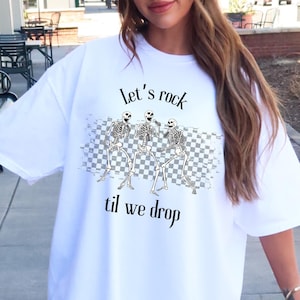 May include: White oversized t-shirt with a graphic of three skeletons dancing on a checkered background. The text "let's rock til we drop" is printed on the shirt.
