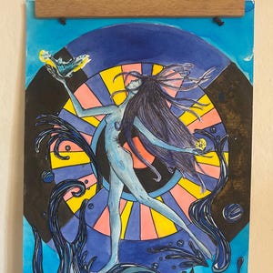 Puede incluir: Obra de arte en acuarela de una figura esbelta con cabello largo y oscuro, sosteniendo un objeto amarillo y azul, sobre un fondo de un diseño de rueda colorido. La figura es de color azul claro, con formas oscuras similares al agua. La obra se exhibe con un colgador de madera.