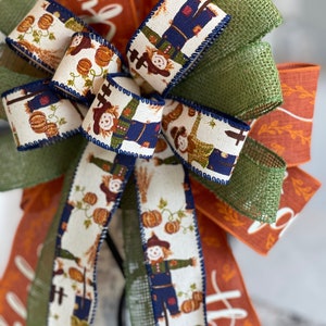 May include: A fall-themed bow with a burlap and green ribbon, and a white ribbon with a pattern of scarecrows and pumpkins. The ribbon has the word "thankful" written on it.
