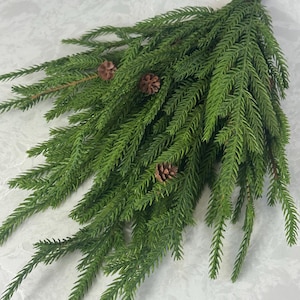 May include: A sprig of artificial greenery with vibrant green needles and small brown pinecones. The stem is a natural brown color. This decorative piece is suitable for seasonal home decor and crafting projects.
